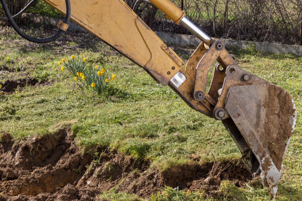 An excavator is digging the ground in the countryside in spring