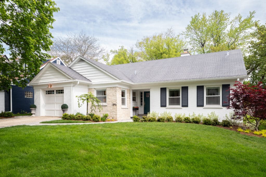 A house with a white brick and brown stone siding and beautiful landscaping.